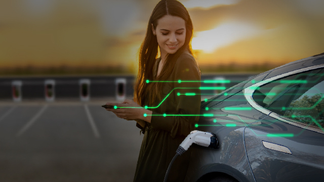 Žena stojící vedle nabíjeného elektromobilu, její telefon je propojen se sítí vozidla