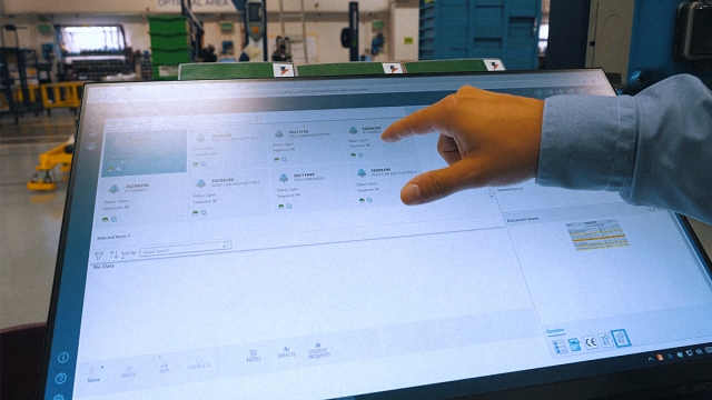A hand interacting with Opcenter Execution Discrete software inside a manufacturing facility.