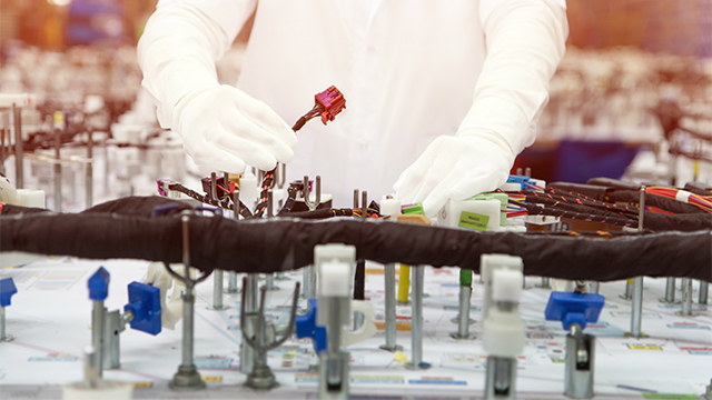 Image of a worker inspecting wire harness connectors in a manufacturing facility