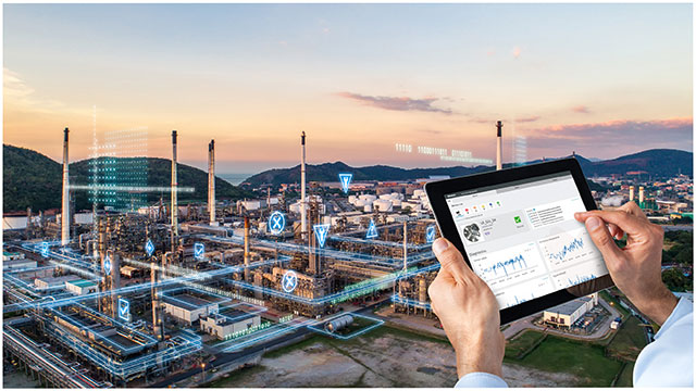 Person holding tablet in front of refinery at sunset.