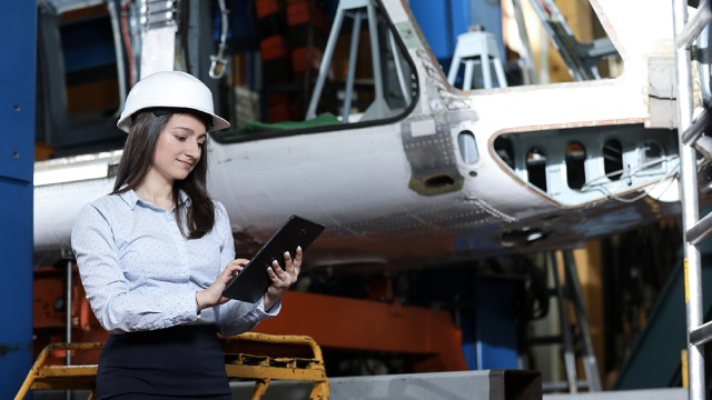 MBSE connects the virtual and physical worlds as an aerospace engineer in a hard hat consults data on a tablet standing beside the physical aircraft.