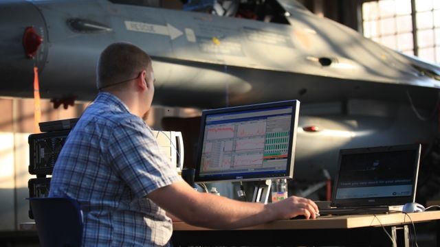 A man is sitting at a desk in front of a computer that shows simulation software for aircraft certification