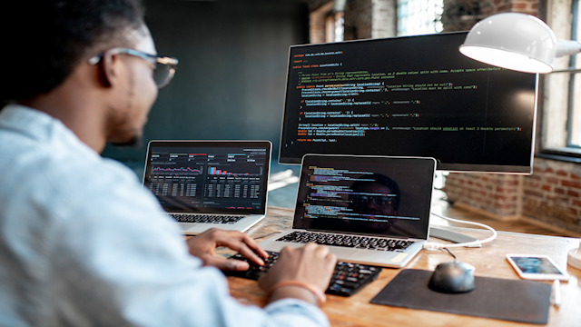 Man codes in front of several computer screens