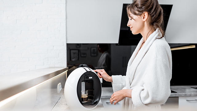Innovation in Home Appliances - Woman in a home kitchen using a coffee machine to brew an expresso coffee.