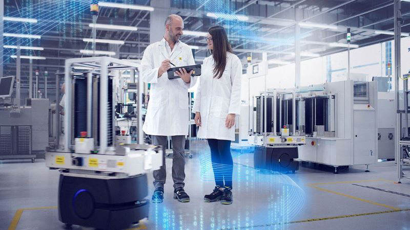 A male manufacturing engineer holding a laptop and collaborating with a female engineer in a lab. 