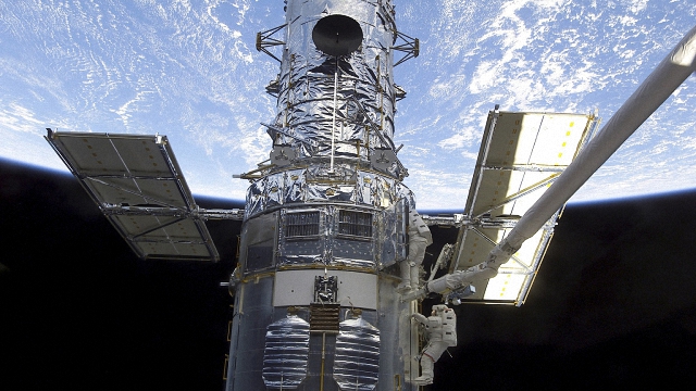 Two astronauts on a space system in orbit. Satellite qualification testing minimizes costly and risky in-orbit repairs.