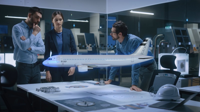 Three people in an office reviewing aerospace technical documents with a model of an airplane over the workstation.